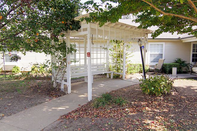 A white pergola covering a walkway surrounded by greenery in a garden setting.