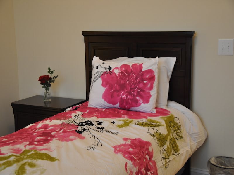 A cozy bedroom with a floral-patterned bedspread and pillow, accompanied by a nightstand with a flower vase.