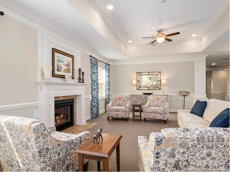 A cozy living room featuring a fireplace, patterned armchairs, and a ceiling fan.