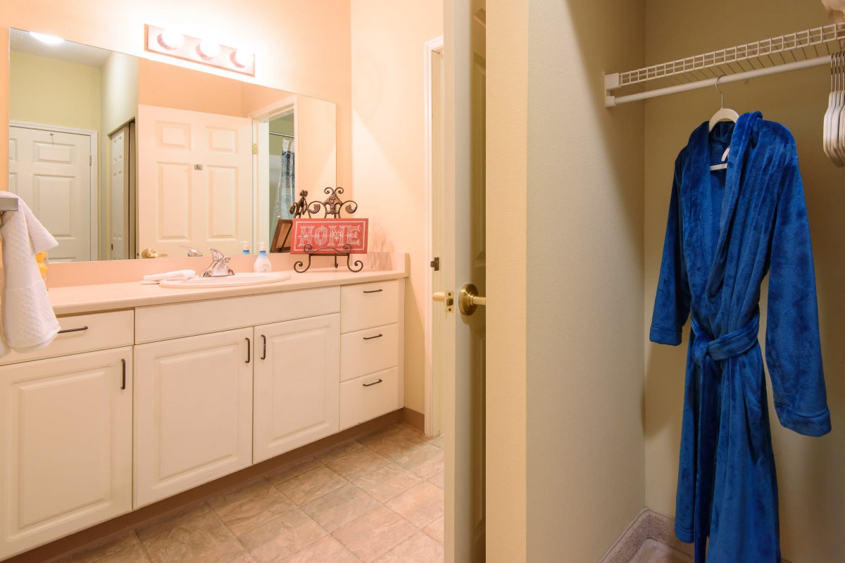 A bathroom with a vanity and a nearby closet featuring a blue robe.