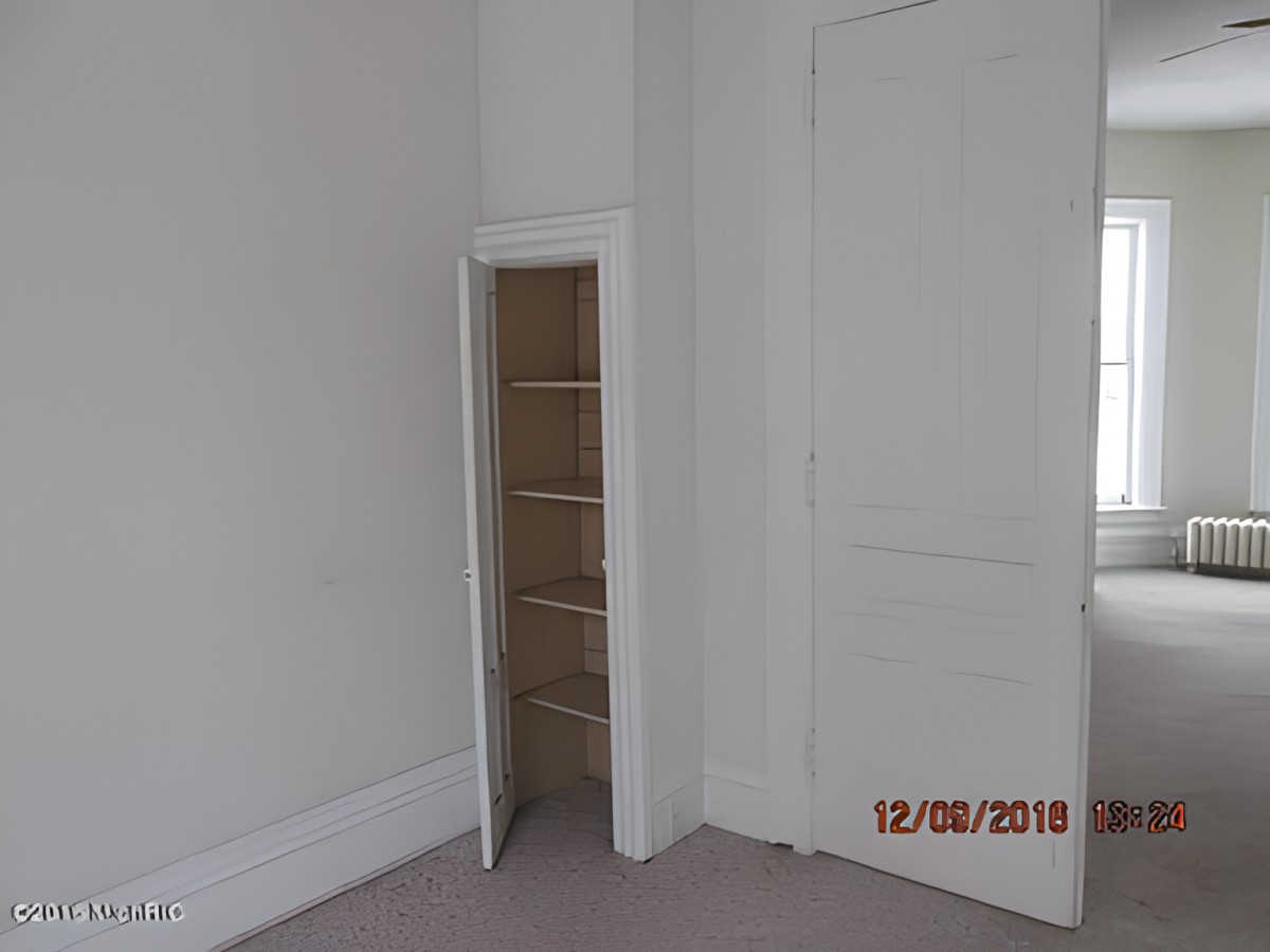 A small closet with shelves in an empty room with white walls.