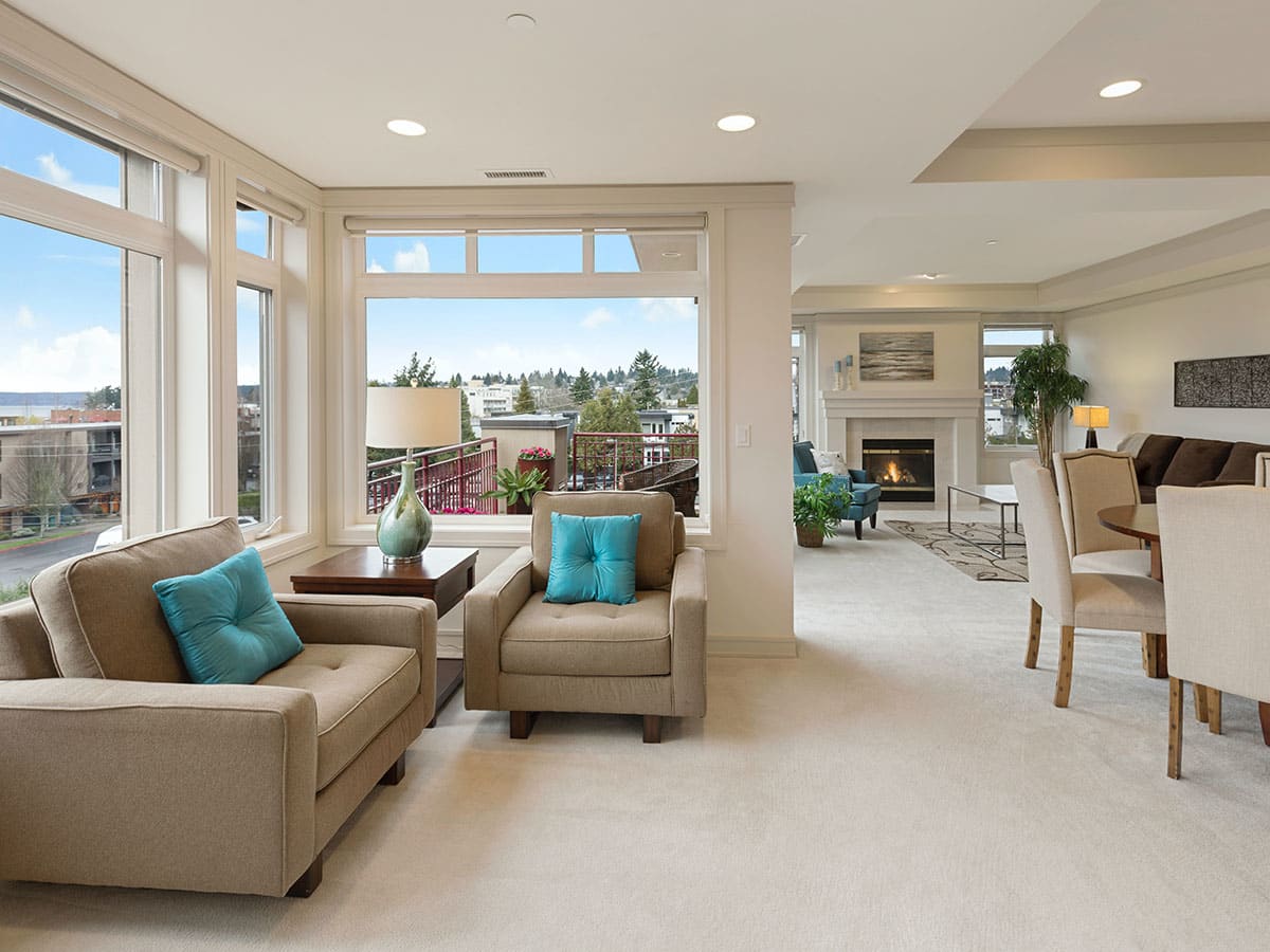 A bright and spacious modern living room with armchairs and a view into the dining area, featuring large windows that let in natural light.