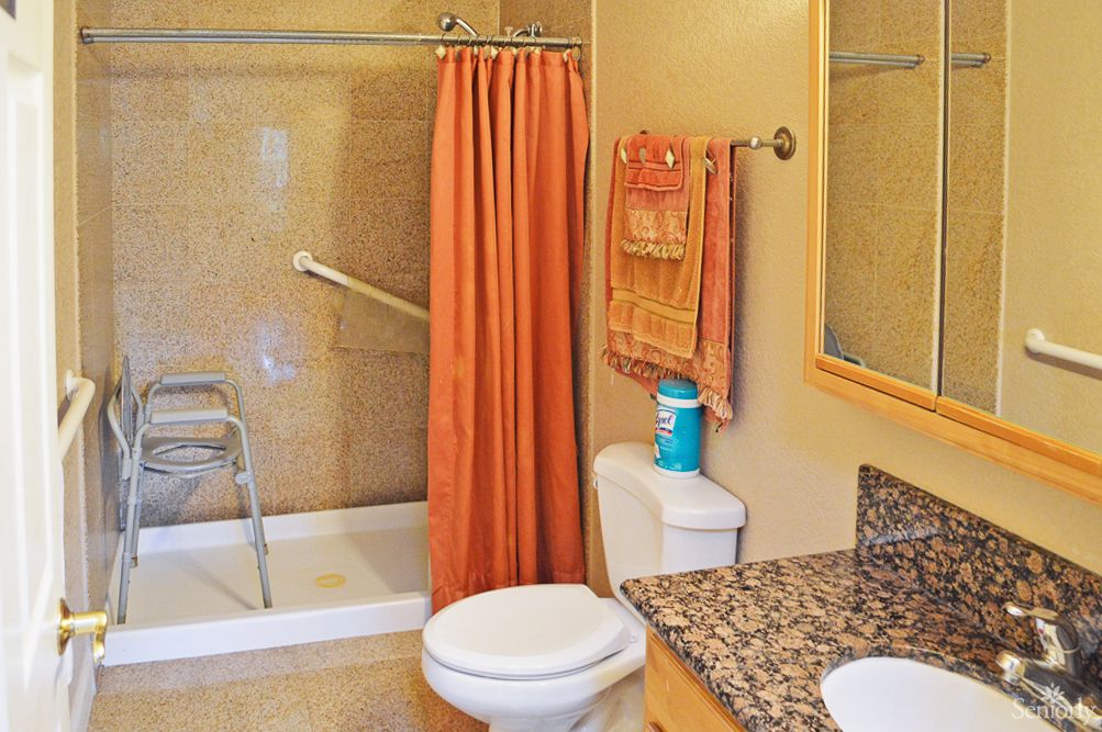 An accessible bathroom with a shower, orange shower curtain, toilet, towels, and grab bar.