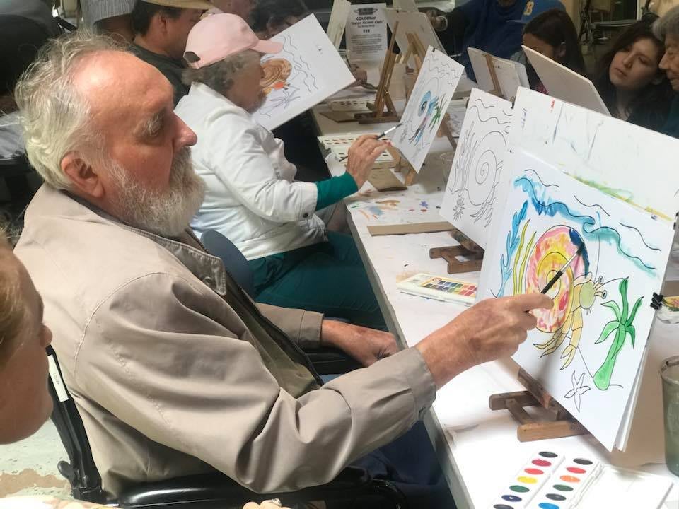 Elderly individuals participating in a group art class, engaging in painting activities.