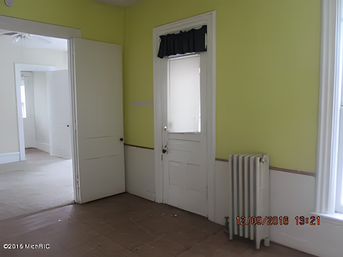 An empty room with yellow walls, featuring two doors and a radiator.