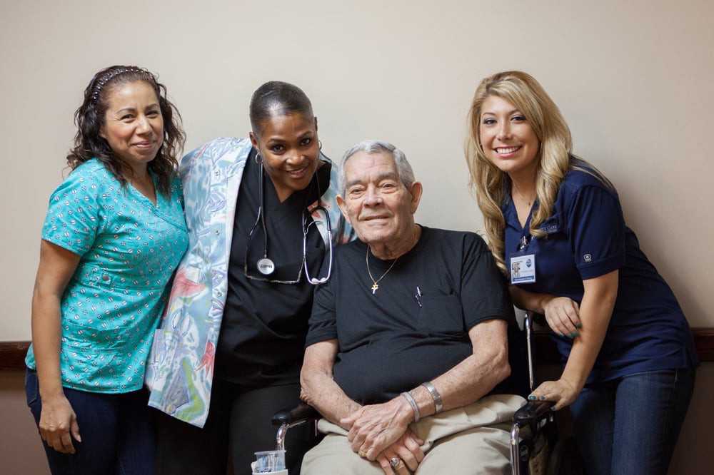 A group of healthcare professionals smiling with an elderly person seated in a wheelchair.