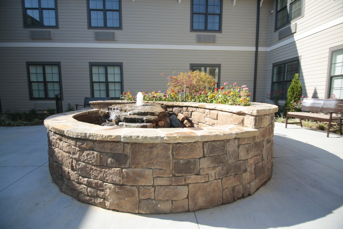 A stone fountain surrounded by a circular brick wall in a courtyard setting.