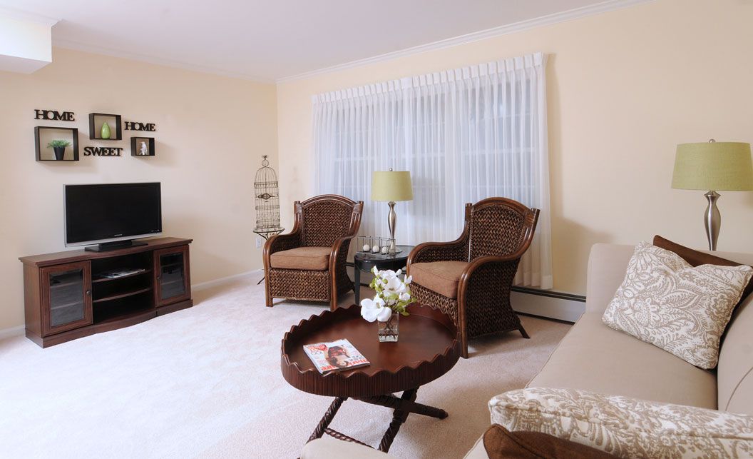 A cozy living room featuring rattan chairs, a round coffee table, and a TV stand with warm lighting.
