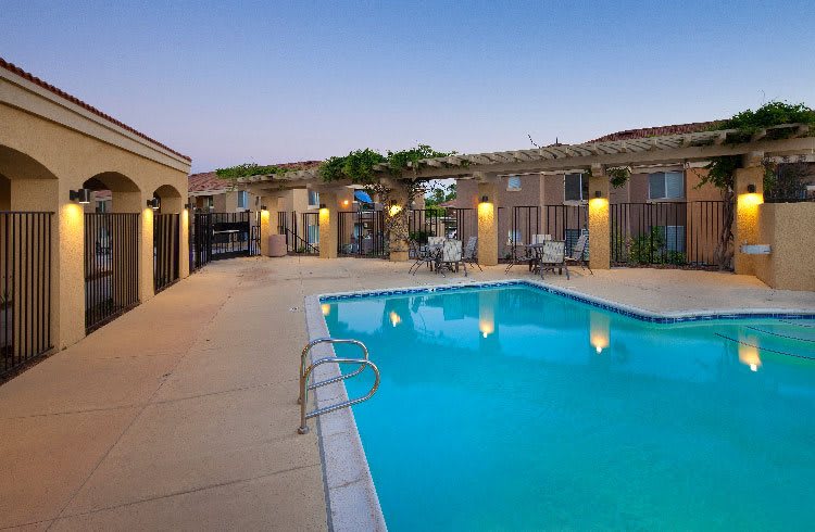 An inviting outdoor swimming pool area with patio seating, illuminated during the evening.