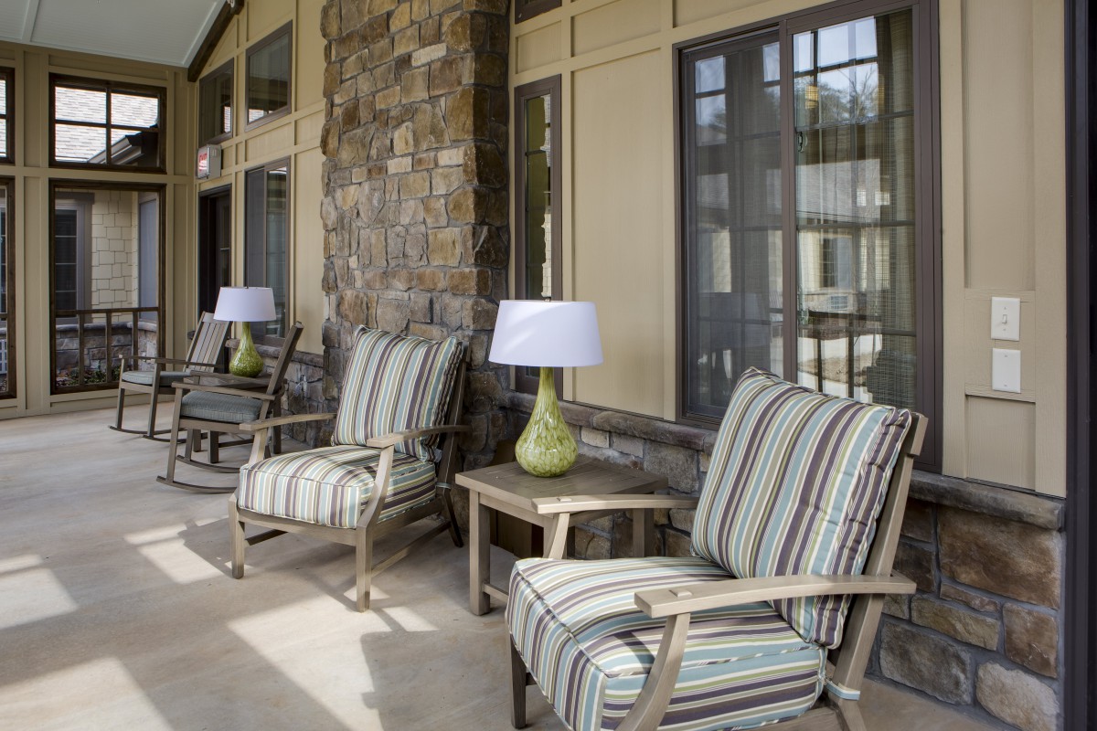 A cozy patio with striped cushioned chairs and small tables with lamps, set against a stone wall.