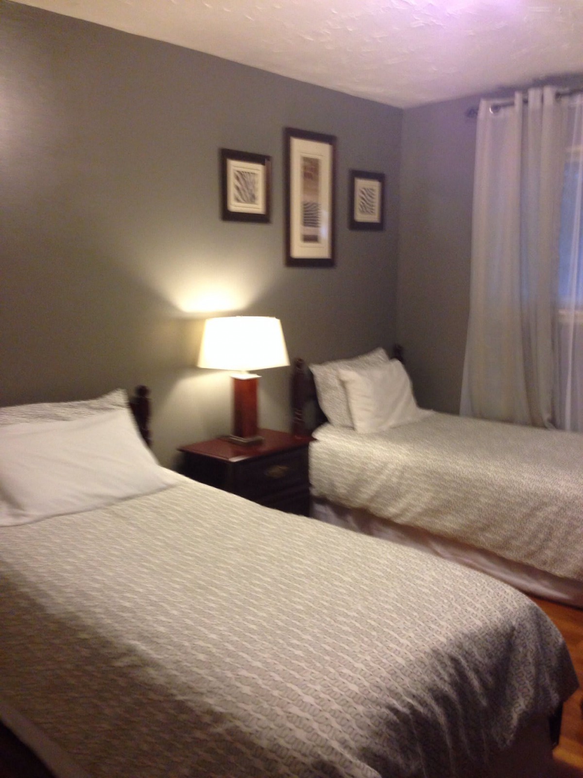 A cozy bedroom with two twin beds, a nightstand with a lamp, and framed art on the wall.