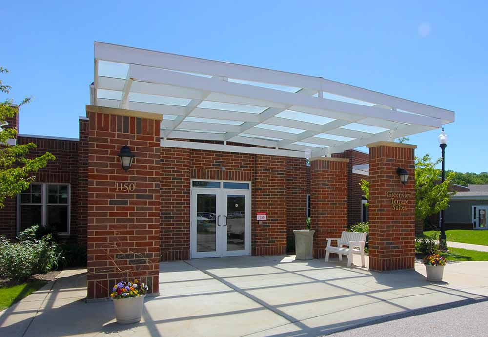 A brick building entrance with a pergola and outdoor seating.