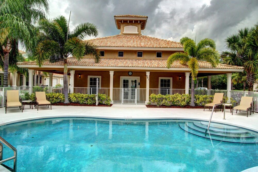 A luxurious house with a swimming pool and palm trees set against a cloudy sky.