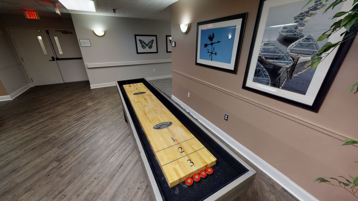 A shuffleboard table in a recreation area with framed wall art.