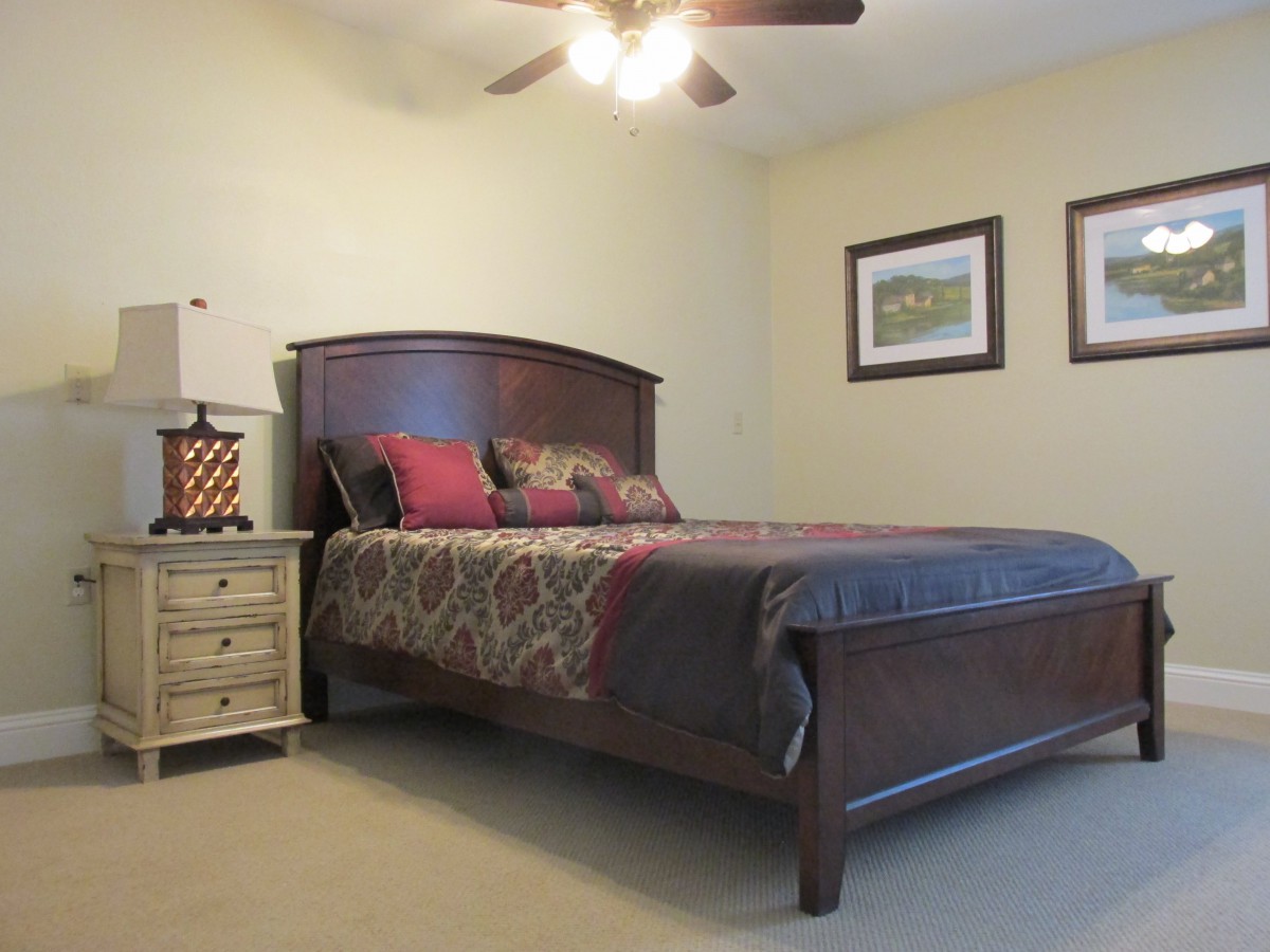 A cozy bedroom featuring a wooden bed with patterned bedding, a nightstand with a lamp, and artwork on the walls.
