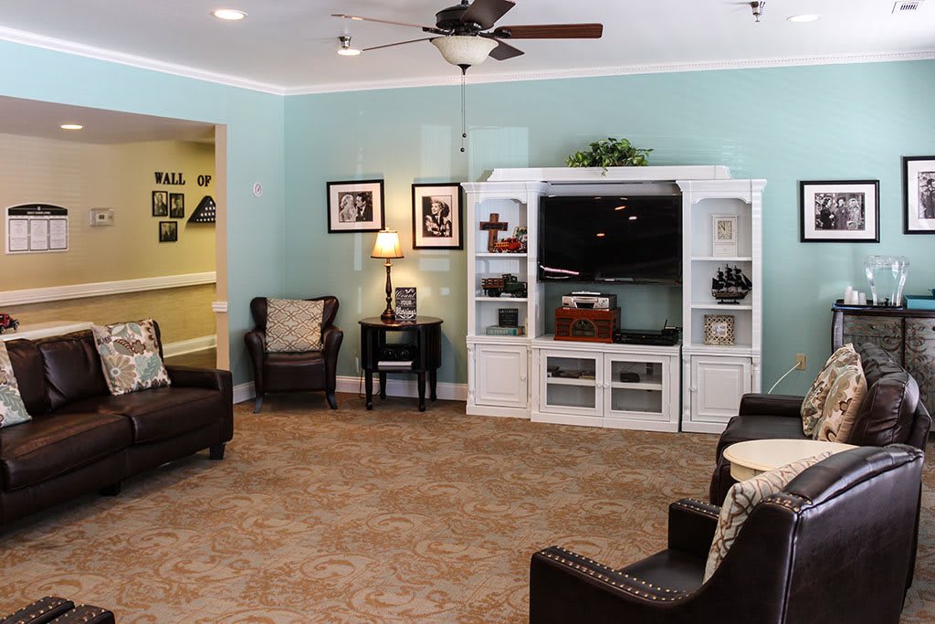A cozy living room with blue walls, featuring a white entertainment cabinet and comfortable leather chairs.