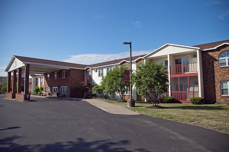 Exterior view of a residential apartment building with a driveway and trees under a clear blue sky.