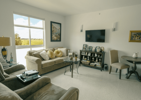 A cozy living room featuring comfortable sofas, an armchair, a large window with scenic views, and a wall-mounted television.