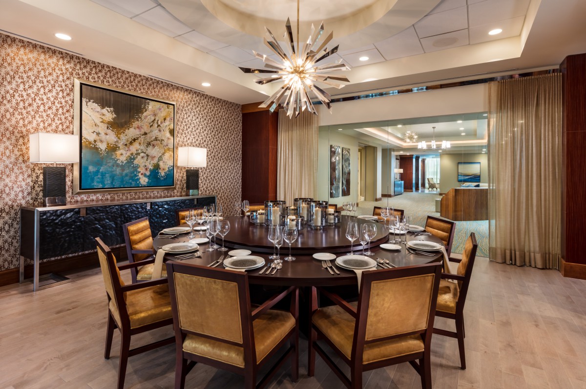 A luxurious dining room featuring a round table set with elegant dinnerware, surrounded by chairs and adorned with a striking chandelier.