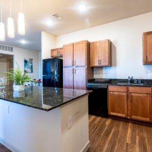 A modern kitchen with a central island, wooden cabinets, and granite countertops.