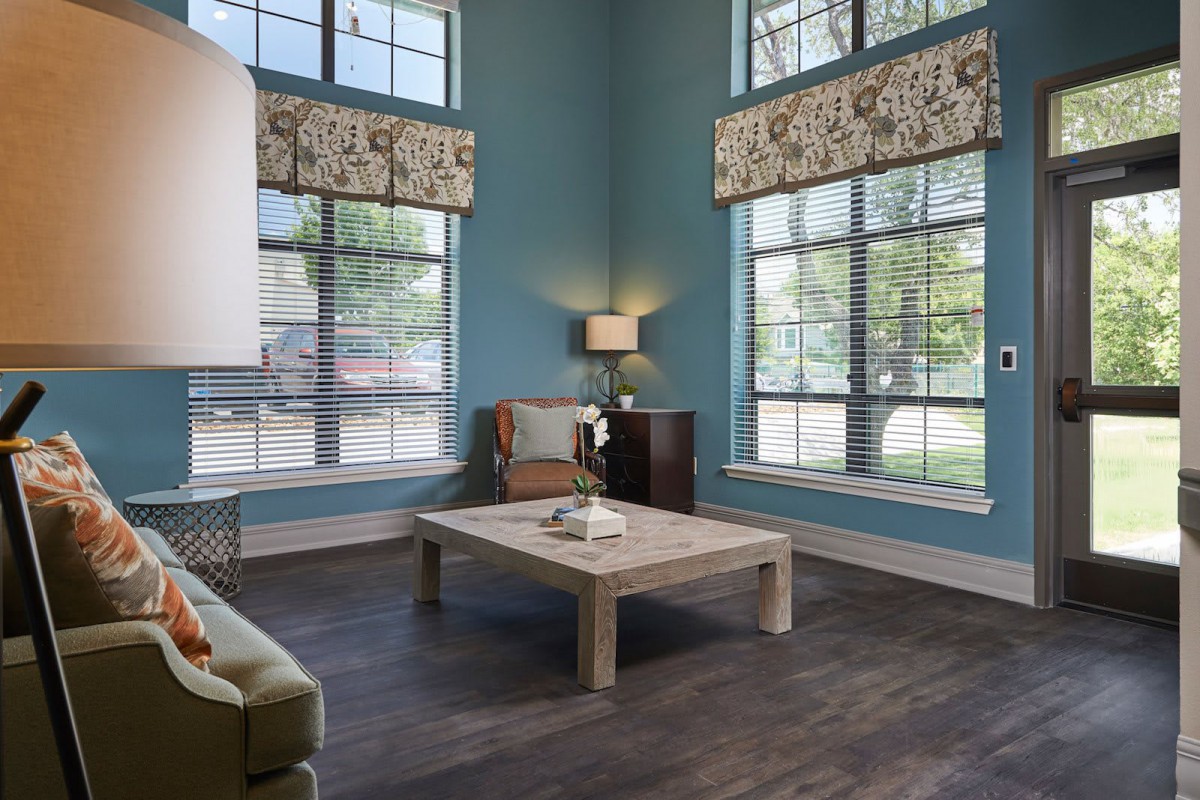 A cozy living room with blue walls, large windows, and a central coffee table.