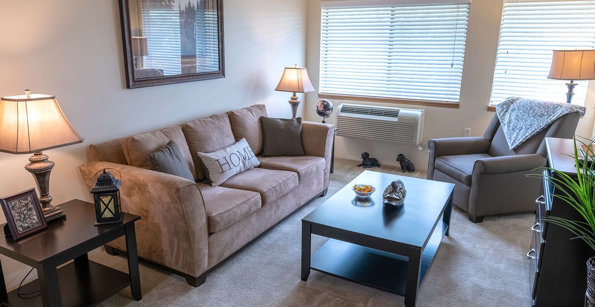 A cozy living room with a sofa, coffee table, and a lamp by the window.