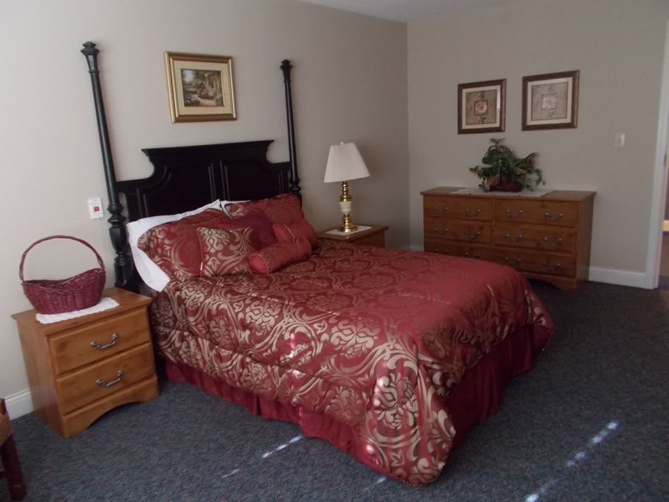 A well-decorated bedroom featuring a bed with red bedding, a side table with a lamp, and framed art on the walls.