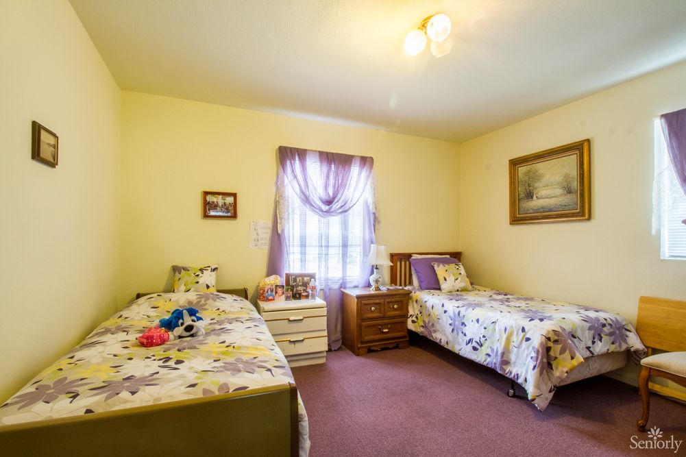 A cozy bedroom features two twin beds with floral bedding, a shared nightstand, and decorative curtains on the window.