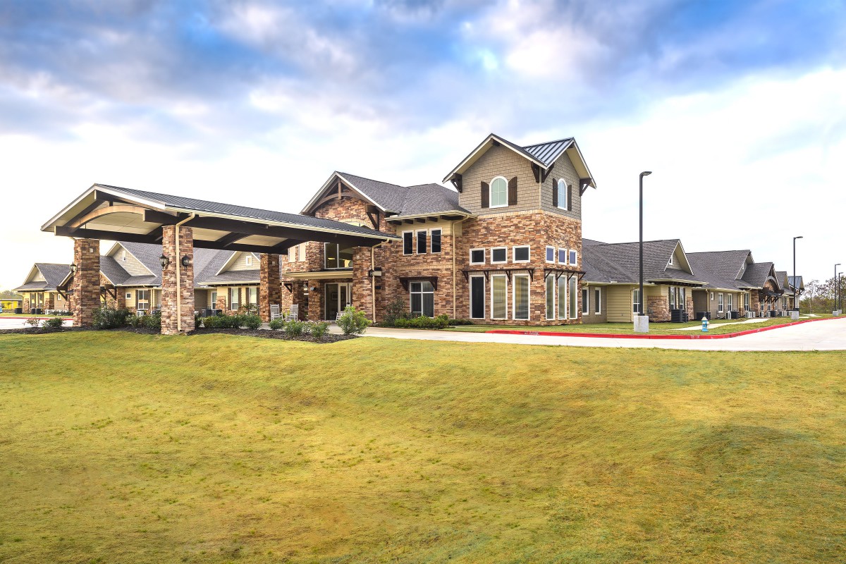 A large brick residential building with a well-maintained lawn under a partly cloudy sky.
