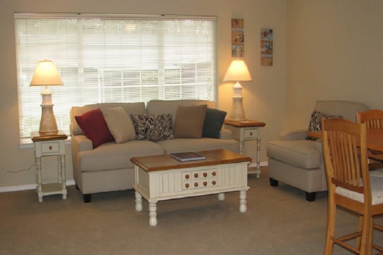 A cozy living room with a sofa, armchair, and coffee table, accented by colorful pillows and a lamp.