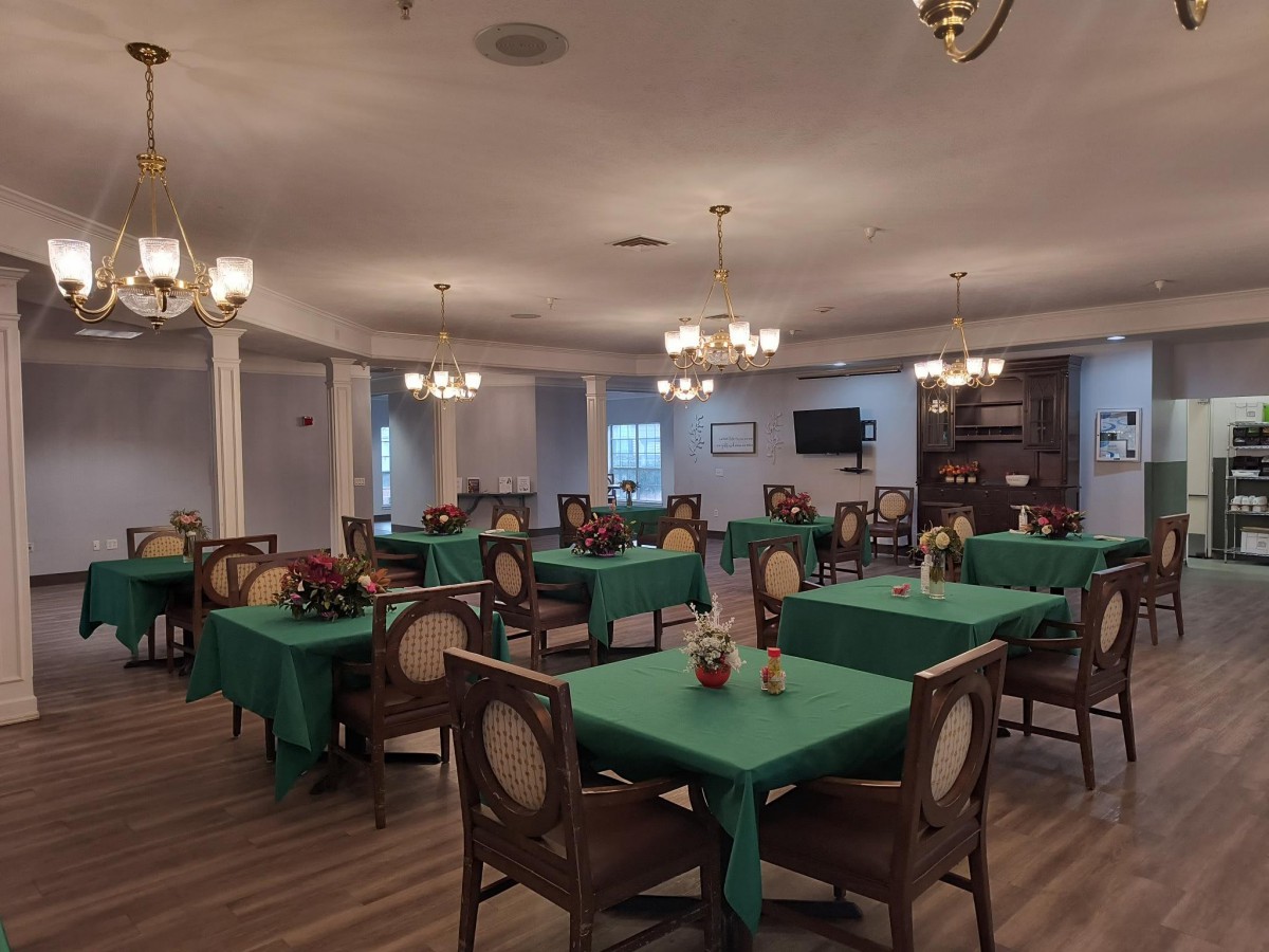 A spacious dining room with green tablecloths and elegant chandeliers.