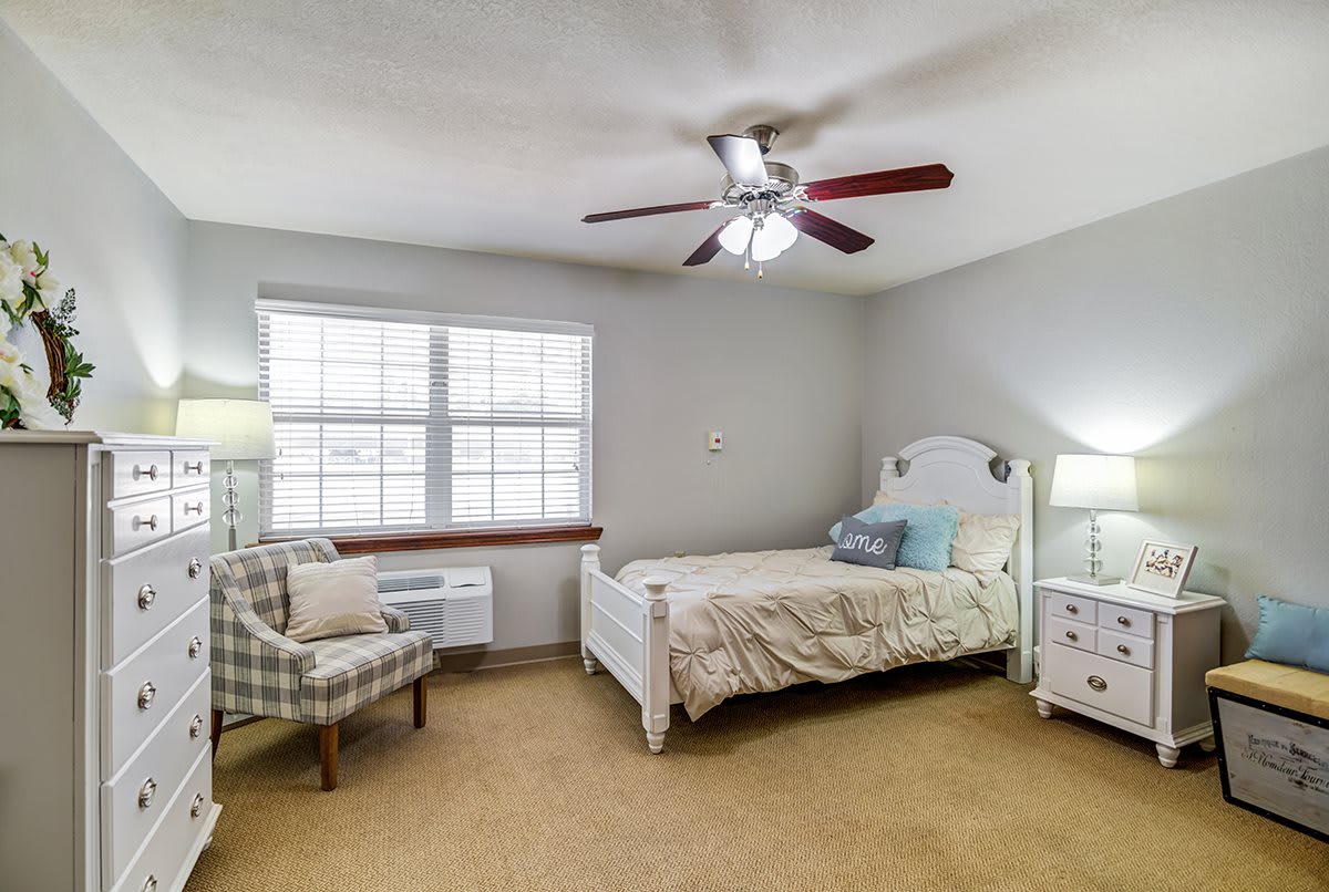 A cozy bedroom with a single bed, ceiling fan, and armchair.