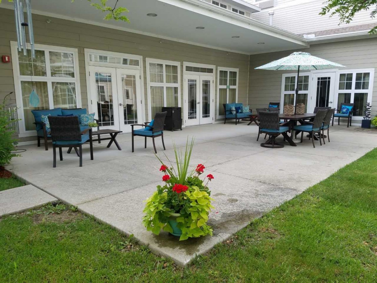 A cozy patio area with outdoor seating, tables, and an umbrella, surrounded by greenery and flowers.