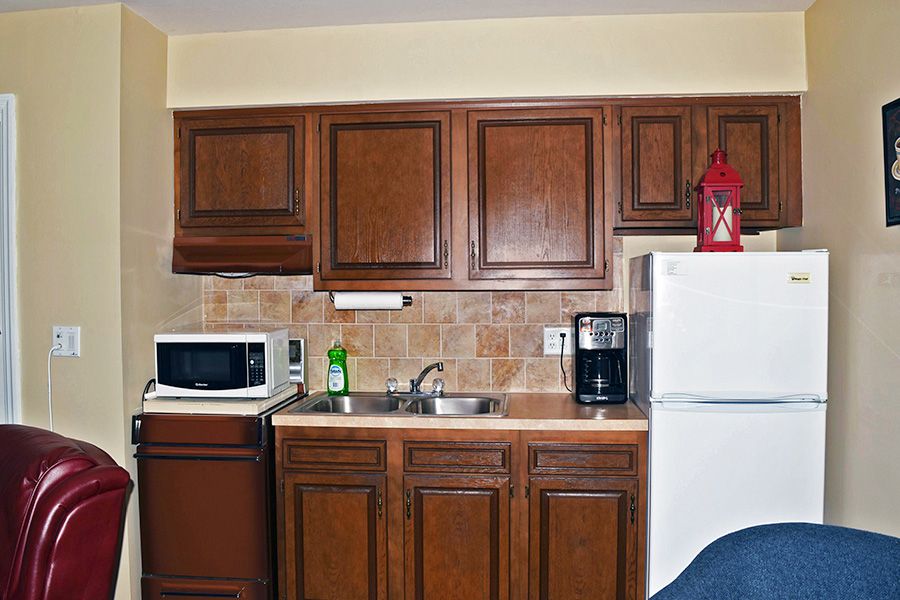 A compact kitchen area with wooden cabinets, a microwave, sink, refrigerator, and coffee maker.