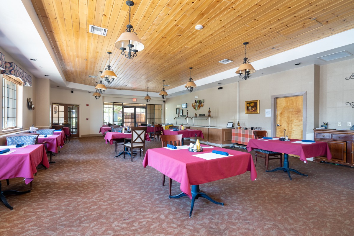 A spacious dining room with red tablecloths and wooden ceiling.