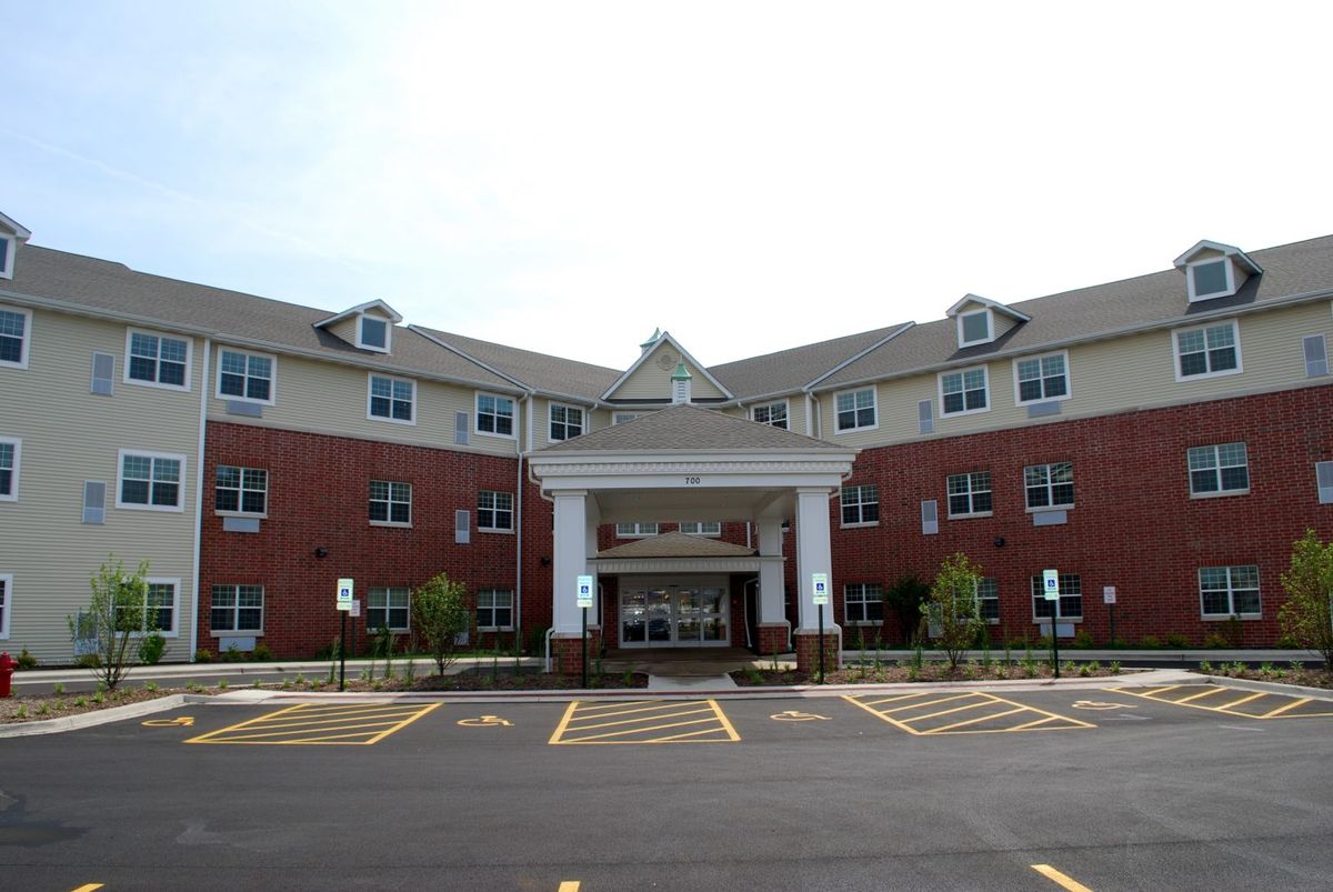 A modern hospital building with a brick facade and an entrance leading to a covered drop-off area, surrounded by a parking lot.