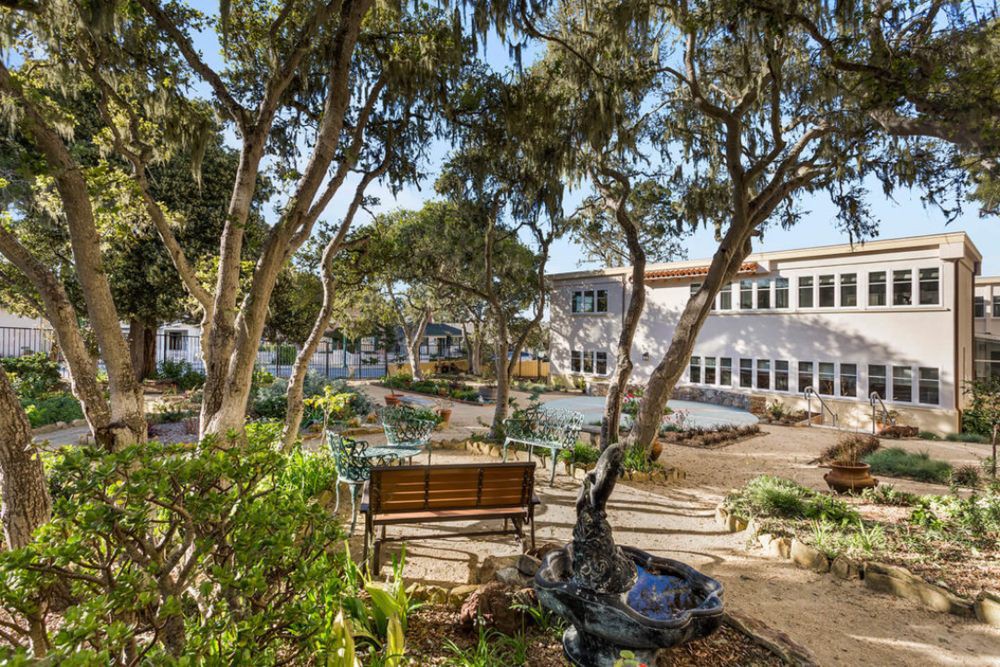 A peaceful garden with benches surrounded by trees and a building in the background.