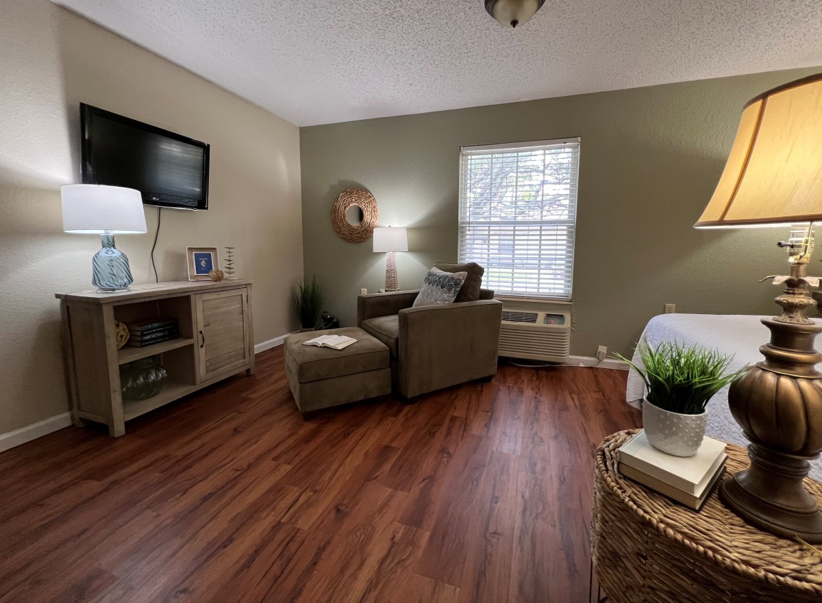 A cozy living room with wood flooring, featuring a comfortable armchair and a television mounted on the wall.