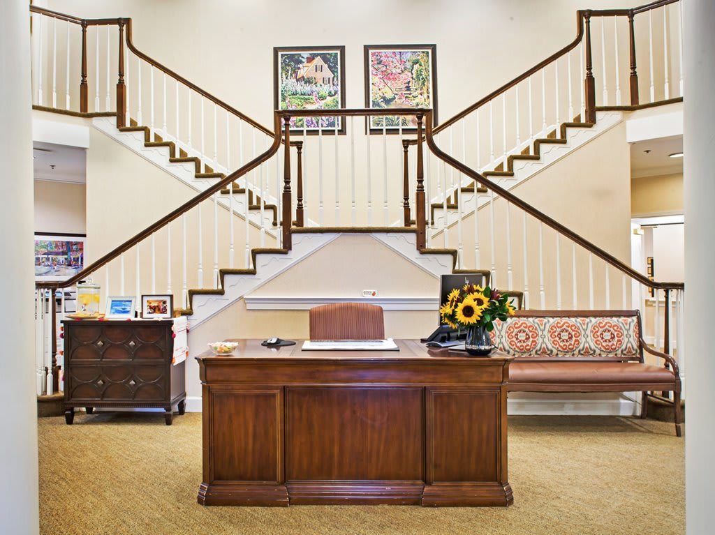 A stylish office interior featuring a wooden desk, decorative art pieces, and a grand staircase.