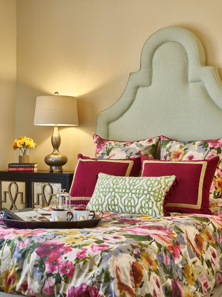 A stylish bedroom featuring floral bedding and decorative pillows, complemented by a modern table lamp and cozy decor.