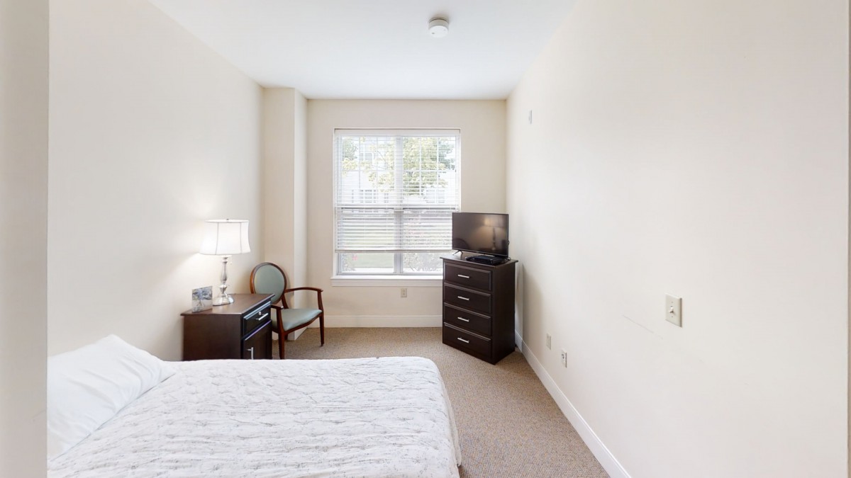 A cozy bedroom with a bed, dresser, and TV near a window.