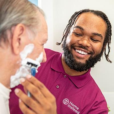 A caregiver assists an elderly person with shaving, creating a supportive and joyful moment.