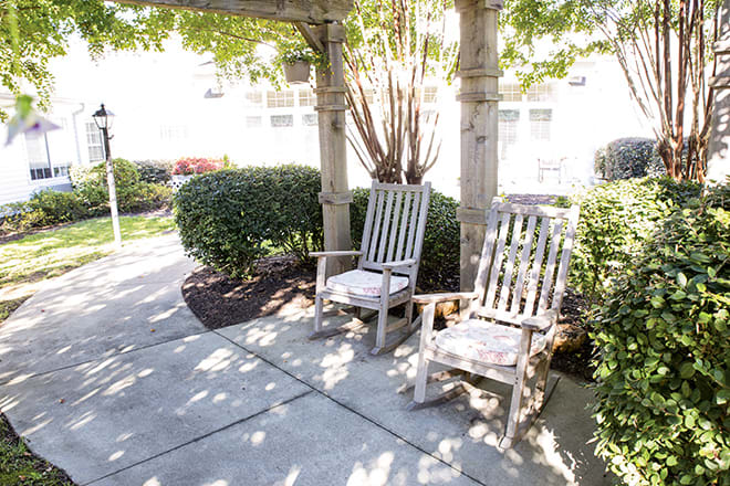 Two rocking chairs on a sunny patio surrounded by lush greenery.
