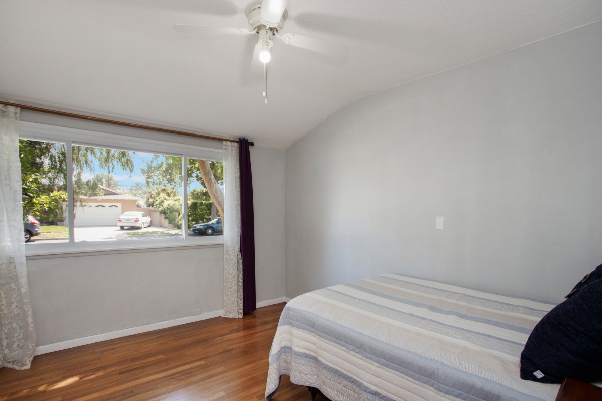 A minimalist bedroom with a bed, hardwood flooring, and large window allowing natural light.