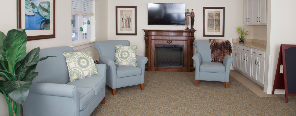 A cozy living room with blue armchairs, a wooden fireplace, and a mounted television.