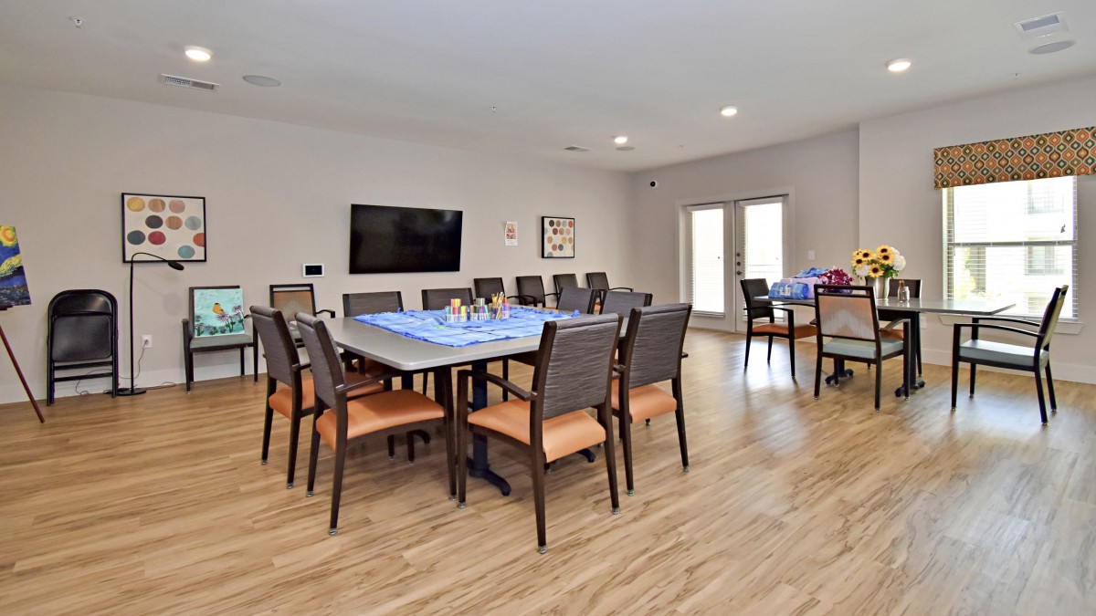 A spacious dining or meeting room with a large table, several chairs, and a wall-mounted television.