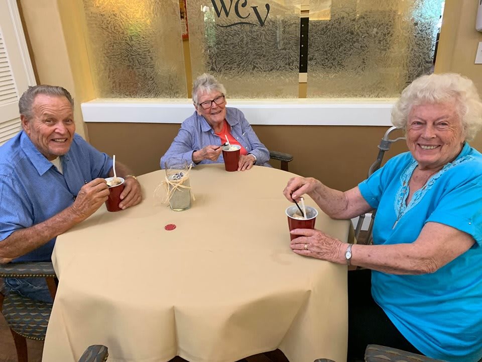 Three elderly individuals enjoying drinks together at a table indoors.