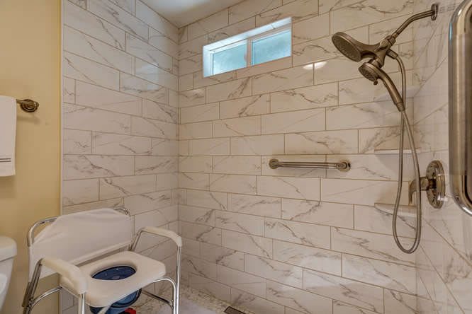 Modern bathroom with marble tiles, featuring a shower head and a safety grab bar.