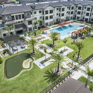 Aerial view of a modern apartment complex featuring a large swimming pool and landscaped gardens.