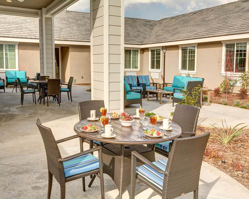 A cozy outdoor patio featuring a dining table set with drinks and snacks, surrounded by comfortable chairs and seating in a courtyard setting.